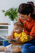 © Jovo Jovanovic/Stocksy - Smiling woman reading picture book  with daughter