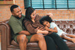 © chokniti - Heartwarming family moment as an African American father and daughter share playful time together on the couch, surrounded by love, laughter, and the warmth of home, while mom gently looks on with joy