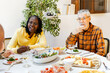 © Jimena Roquero/Stocksy - Diverse senior friends gathered together around dining table