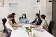 © fizkes - Professional team take part in meeting in office boardroom. Five businesspeople sit around conference table, engaged in discussion, brainstorming, strategizing, or reviewing important business topics
