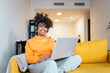 © Santi Nuñez/Stocksy - Young woman working from home on laptop and wearing headphones.
