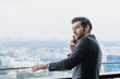 © Jack Tamrong - Handsome male executive businessman talking on phone in office balcony with blurred skyscraper downtown view