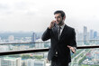 © Jack Tamrong - Handsome male executive businessman talking on phone in office balcony with blurred skyscraper downtown view