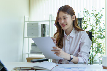 smiling businesswoman reviewing financial reports at desk, with charts and graphs in a modern office