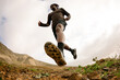 © Adrian Rodd/Stocksy - Wide shot from low angle of a runner crossing a rocky trail