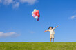 © mei - A little girl is playing with a balloon on the grass under the blue sky and white clouds