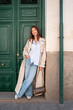 © Santi Nuñez/Stocksy - Young tourist woman leaning against a green door is smiling at camera