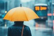 © pingpao - A person stands under a yellow umbrella in the rain, waiting near a blurry city bus on a wet street.