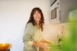 © Johnér - Happy curly haired woman looking away while washing dishes in sink at kitchen