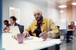 © Johnér - Focused bald male entrepreneur writing notes while working on laptop in office