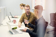 © Johnér - Young corporate employee asking questions to male manager while sitting with laptop at desk in office