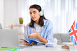 © Pixel-Shot - Young woman in headphones learning English language online at home