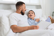 © Pixel-Shot - Happy father with his son in pajamas reading book on bed at home