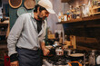 © qunica.com - A man preparing food in a warmly lit, rustic-style kitchen. Ingredients, pots, and utensils are displayed, creating a homely and inviting culinary scene.