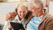 © peopleimages.com - Senior couple, tablet and happy on sofa in home with hug, laughing and relax with film in living room. Elderly man, woman and digital touchscreen with app for movies, comedy and video in retirement