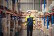 © Wanwajee - A white male warehouse worker walks through storage aisles, inspecting shelves while holding a laptop for inventory tracking.