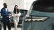 © wedmoments.stock - A car sales manager shows a vehicle to a customer in a luxurious dealership. Concept a premium car-buying experience that combines expert guidance with high-end service in an elegant setting.