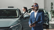 © wedmoments.stock - A couple during the purchase of a modern new car accompanied by a black salesman in a car dealership. Concept of a long-awaited purchase, sale and test drive of a new car.