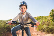 © WavebreakMediaMicro - Boy wearing polka-dot helmet riding bicycle along sunlit dirt trail between shrubs under clear sky