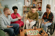 © Seventyfour - Diverse group of young adults including Black woman and Caucasian man and woman with disability in wheelchairs sitting together around table playing board game, during birthday celebration
