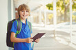 © WavebreakMediaMicro - Boy student standing on sunny covered walkway next to building holding tablet wearing backpack