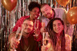 © Seventyfour - Portrait of diverse group of young adults and one Black woman smiling and holding champagne glasses toward camera, during birthday celebration with metallic streamers and balloons