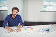 © WavebreakMediaMicro - Man arranging color wheel chart and design sheets at modern office desk while using laptop