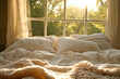 © gyana08 - Unmade bed in warm morning sunlight with soft pillows and a knit blanket by a large window overlooking green trees