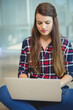© WavebreakMediaMicro - Woman in twenties sitting cross-legged on carpeted floor at modern lounge using silver laptop