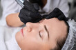 © TRAVELARIUM - Beautician applies permanent makeup to young woman eyebrows in salon. Focus is on precision and artistry, with calm ambiance enhancing experience