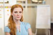 © WavebreakMediaMicro - Red-haired woman in twenties sitting in office chair with glass wall sticky notes and flip chart