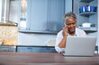 © wavebreak3 - Senior African American woman juggling smartphone and laptop at kitchen counter, copy space