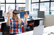 © WavebreakMediaMicro - Office worker wearing VR headset raising hands at open plan office desk with laptop and monitors