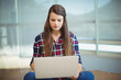 © WavebreakMediaMicro - Woman sitting cross-legged on bench holding silver laptop in lounge with roller-shade windows