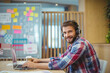 © WavebreakMediaMicro - Mid adult man with headphones using laptop with coffee at office desk beside whiteboard, copy space