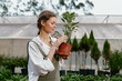 © SHOTPRIME STUDIO - Young woman in casual wear caring for a potted plant in a greenhouse, showcasing her passion for gardening and nature s beauty