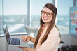 © WavebreakMediaMicro - Female office worker holding silver laptop near window wearing eyeglasses by pinboard, copy space