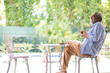 © wavebreak3 - Senior African American man sitting at metal bistro table on backyard patio holding cup, copy space