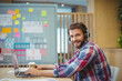 © WavebreakMediaMicro - Man sitting at table in shared space wearing headphones using laptop, planning board, copy space