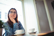 © Wavebreak Media - Woman in denim jacket gazing through café window with white cups and plant, copy space