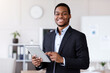 © Prostock-studio - Smiling black entrepreneur young man holding digital tablet, using modern technologies in business, office interior, copy space. Cheerful african american businessman using app for business