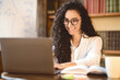 © Prostock-studio - Freelance Concept. Portrait of smiling woman in eyeglasses using and working on computer, typing on laptop keyboard. Young lady sitting at desk with open notebook and doing work project