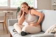 © Pixel-Shot - Upset young woman in tight pants sitting on sofa at home. Weight gain concept