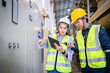 © Sumala - Two engineers wearing insulated safety helmets and vests inspect electric switchgear in gas insulated substation field while discussing grid operations with tablet and radio device