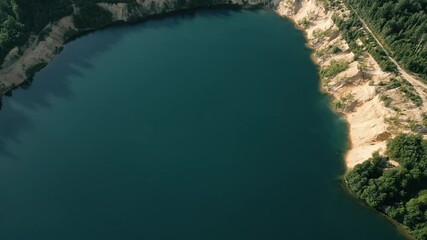 Wall Mural - Aerial footage of a tranquil lake surrounded by dense green woods on a clear sunny day