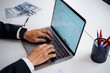 © tech - Person typing on a laptop keyboard wearing a dark suit and smartwatch, working on emails in a bright modern office setting with stationery and documents on the white desk