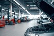 © ttonaorh - Car repair shop, a grey with an open hood in the foreground and other cars on lifting platforms for maintenance in the background. Car service center interior. Blurred background of a car workshop.