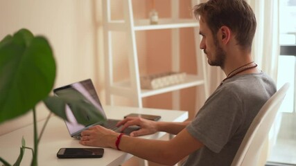Poster - A young man sits at a clean desk in a bright room, intently typing on his laptop. The space blends productivity and modern workspace aesthetics, highlighting contemporary work environments