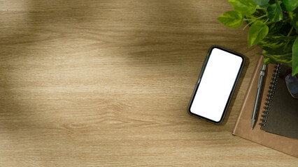 Wall Mural - Top view of smartphone with blank screen, spiral notebooks, and potted plant on wooden desk.