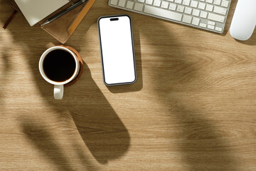 Wall Mural - Office table with blank screen mobile phone, coffee mug, planner, and keyboard under soft morning shadows.